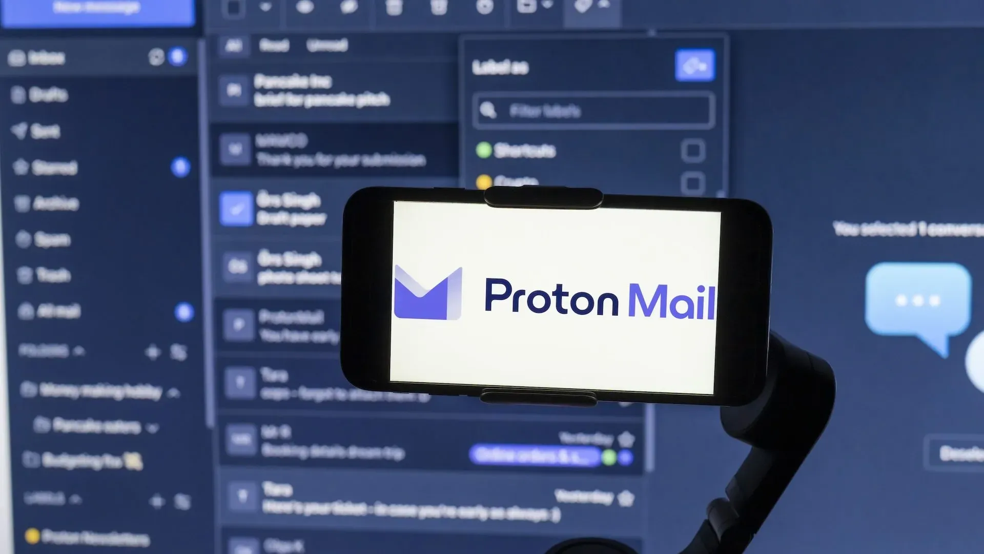 Логотип ProtonMail на экране мобильного телефона с интерфейсом веб-сайта на заднем плане.